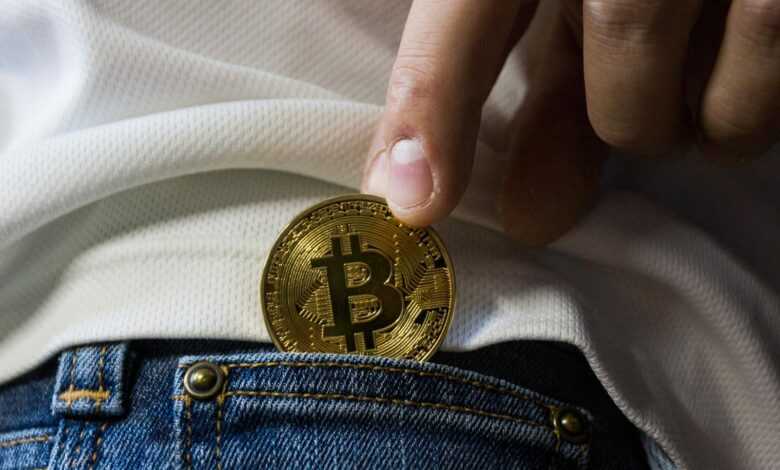 Close-up of hand putting Bitcoin in jeans pocket symbolizing cryptocurrency savings.